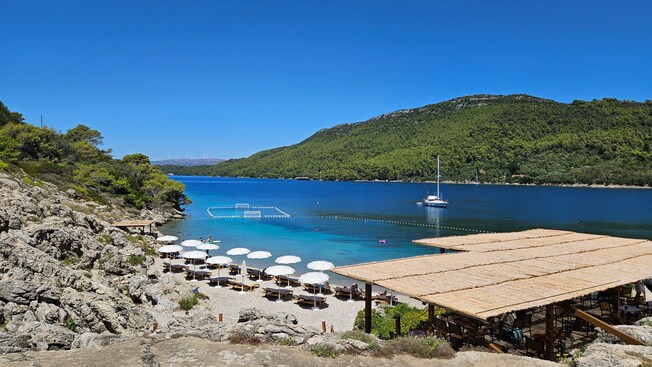 Una pequeña playa con sombrillas y camastros junto al agua y la costa rocosa de una bahía en Dubrovnik, Croacia