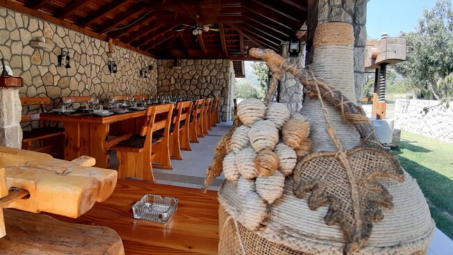 Área de comedor exterior cubierta con vigas de madera a la vista y una larga mesa de madera con sillas