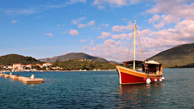 A wooden boat floating on calm water near the dock with hills and houses lining the shore