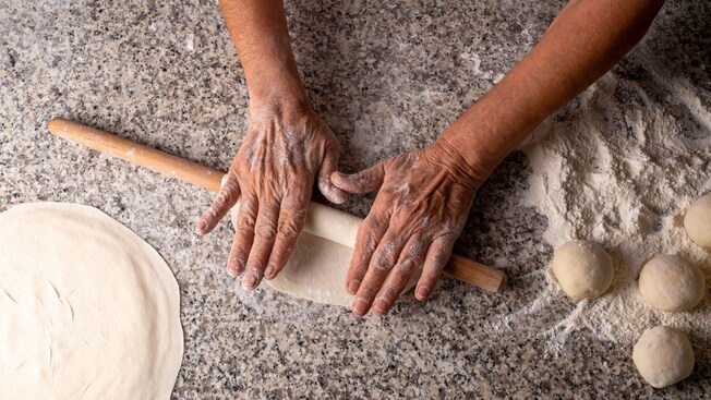 Two hands kneading dough on a floured surface