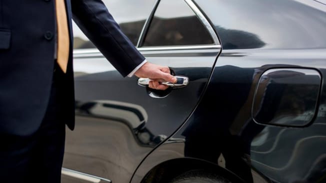 A professional driver in a suit opening the rear door of a luxury sedan A professional driver in a suit opening the rear door of a luxury sedan