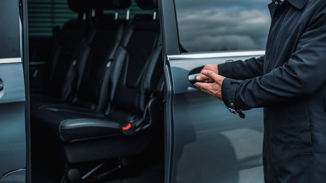 A private driver opening the door of a luxury minivan A private driver opening the door of a luxury minivan