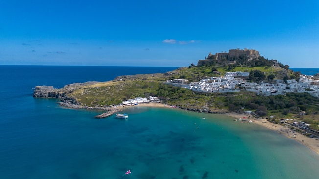 Aerial view of a bay in Rhodes, Greece, with beaches, coastal buildings and Lindos Acropolis on a hill