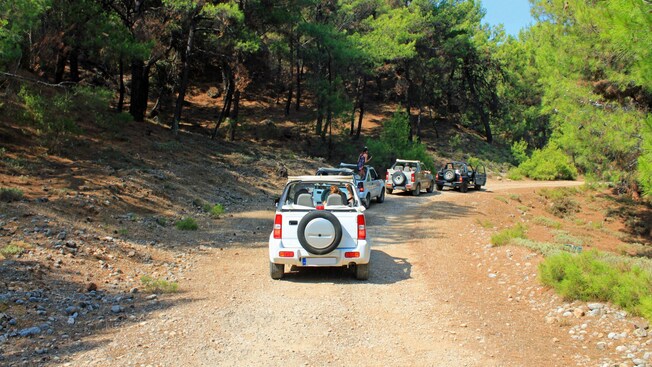 Open air 4 by 4 jeeps traveling along a dirt road through a forested area in Rhodes