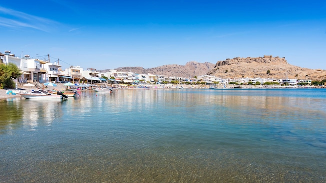 A calm waterfront in Rhodes with small boats, seaside buildings and a hilltop fortress