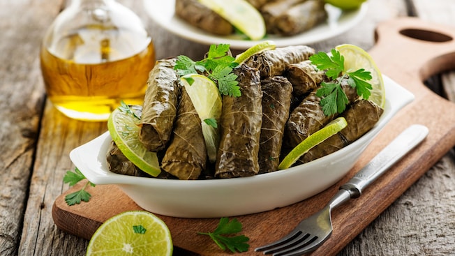 A dish of stuffed grape leaves garnished with lime wedges and parsley on a wooden table
