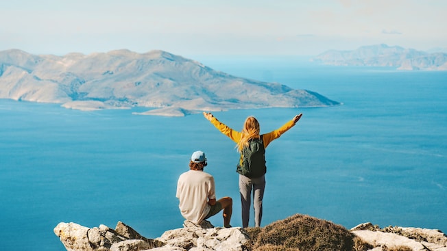 Two hikers on a rocky summit of Akramitis Mountain in Rhodes, Greece, overlooking the Aegean Sea