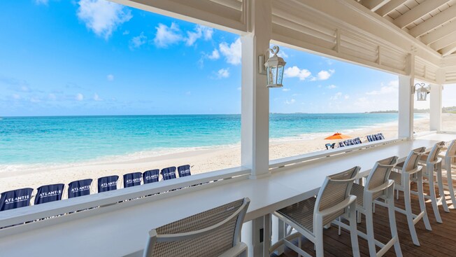 Chairs at a covered patio bar facing a beach with lounge chairs