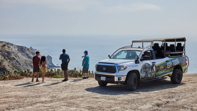 Three Guests and a guide standing on a cliffside overlooking the ocean near an open air tour truck with the words, ‘Catalina Island Conservancy Eco Tour’ Three Guests and a guide standing on a cliffside overlooking the ocean near an open air tour truck with the words, ‘Catalina Island Conservancy Eco Tour’