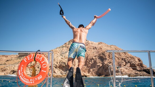 A man in flippers holding snorkeling gear jumps from a boat into the water