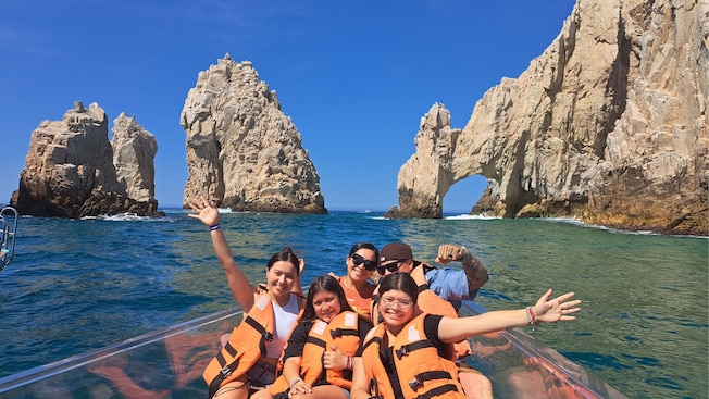 A family posing at the bow of a translucent boat in front of The Arch of Cabo San Lucas A family posing at the bow of a translucent boat in front of The Arch of Cabo San Lucas