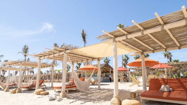 Cabañas con camas de día, hamacas, camastros, mesas y toallas en un club de playa