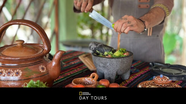 A chef preparing guacamole in a stone bowl during a cooking class in Cozumel, Mexico