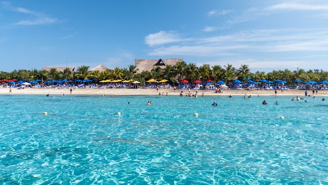 A populated beach with lush foliage, umbrellas and calm waters A populated beach with lush foliage, umbrellas and calm waters