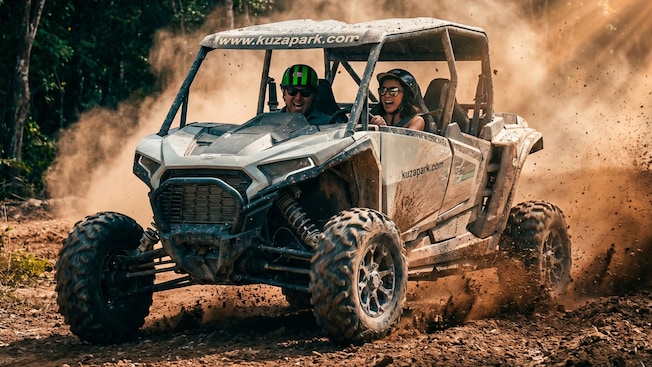 2 Guests in helmets taking a drive in a dune buggy amid swirls of dust at Kuza Beach Park