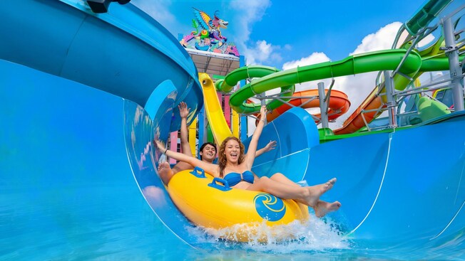 A smiling couple riding an inflatable tube down a water slide at KUZA Waterpark in Cozumel
