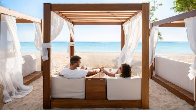 A couple enjoying drinks and relaxing in a cabana facing the ocean A couple enjoying drinks and relaxing in a cabana facing the ocean