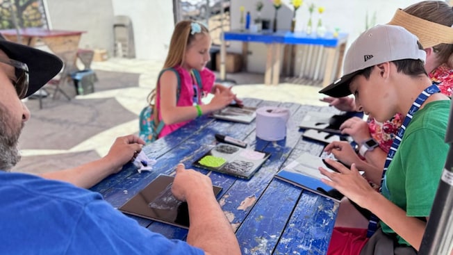 Visitantes en una mesa de pícnic al aire libre con sombra pintando baldosas de cerámica Visitantes en una mesa de pícnic al aire libre con sombra pintando baldosas de cerámica