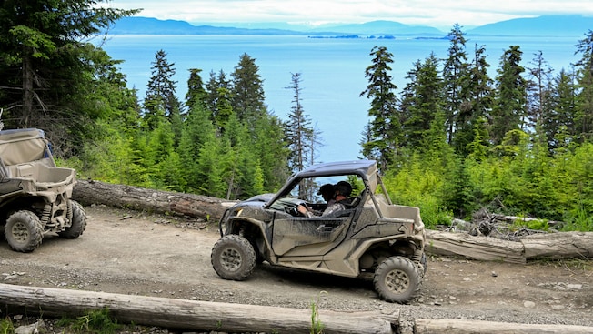 Guests driving UTVs along a dirt trail overlooking Icy Strait Guests driving UTVs along a dirt trail overlooking Icy Strait