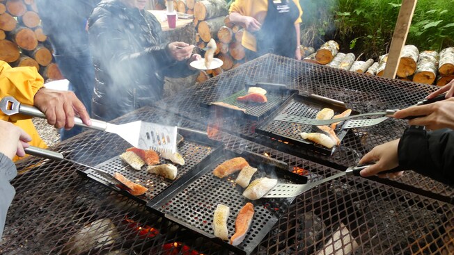 Multiple people grilling fresh fish on a large outdoor grill