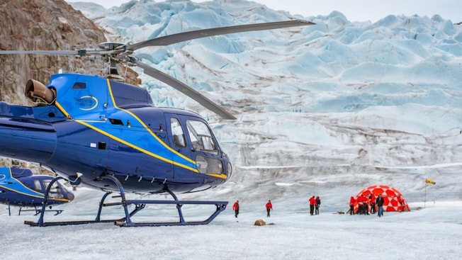 Two helicopters are parked on the glacier, while people gather near a large domed tent Two helicopters are parked on the glacier, while people gather near a large domed tent