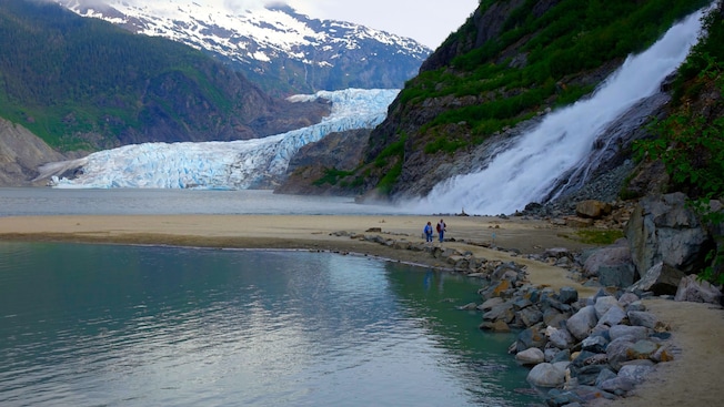 Two people walking on a shore near Mendenhall Glacier and Nugget Falls Two people walking on a shore near Mendenhall Glacier and Nugget Falls
