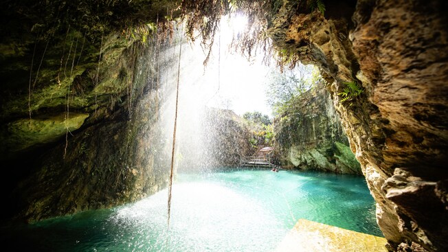 A cenote with a waterfall cascading into the water viewed from inside a cave
