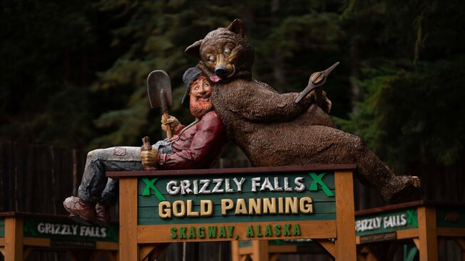 A sign for Grizzly Falls Gold Panning in Skagway, Alaska featuring a prospector and a bear