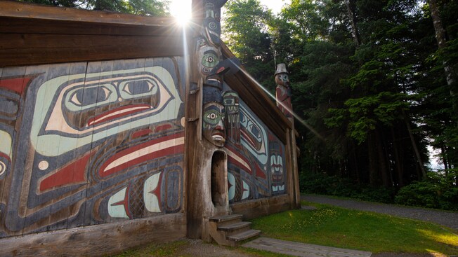 A wooden cultural building featuring totem poles and a mural at Saxman Native Village