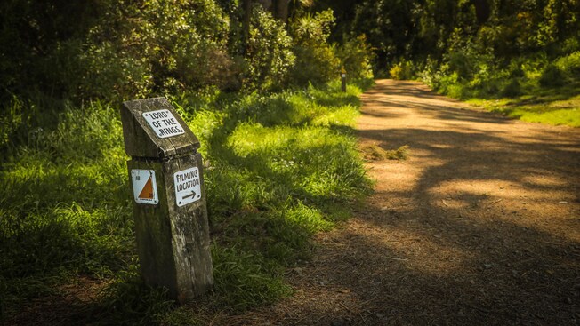 Un camino de tierra rodeado de frondosa vegetación y un letrero que dice “Lugar de rodaje de El Señor de los Anillos”