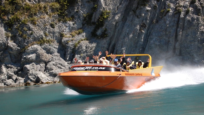 Guests wearing life jackets riding a jet boat at high speed near rocky cliffs Guests wearing life jackets riding a jet boat at high speed near rocky cliffs