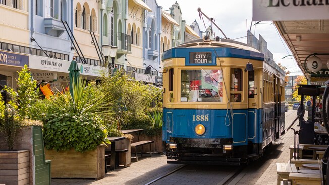 Car number 1888 of the Christchurch Tram operating on the city tour by shopfronts and outdoor seating areas