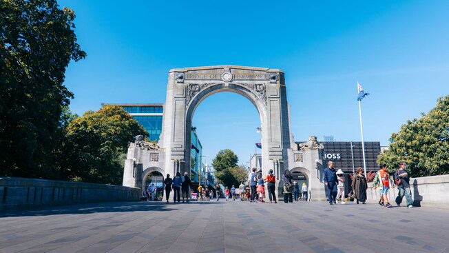 People walking beneath the Bridge of Remembrance, a stone arch monument in Christchurch, New Zealand