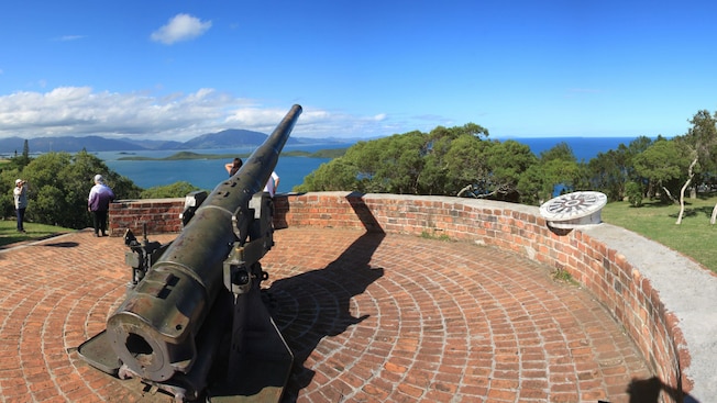 A cannon mounted on a circular brick platform overlooking the ocean with lush greenery and distant mountains A cannon mounted on a circular brick platform overlooking the ocean with lush greenery and distant mountains
