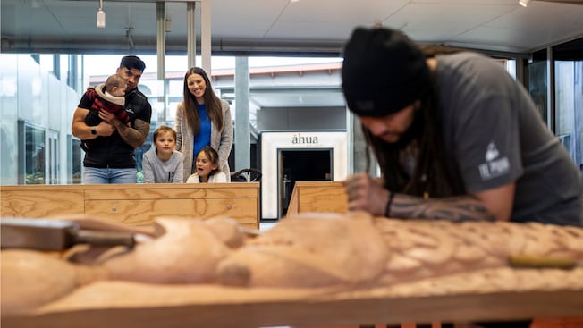 A family of Guests watching a Māori wood carver at work A family of Guests watching a Māori wood carver at work