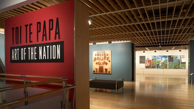 The entrance to a gallery with wooden floors and artwork displayed on the walls and the words ‘Toi Te Papa, Art of the Nation’ The entrance to a gallery with wooden floors and artwork displayed on the walls and the words ‘Toi Te Papa, Art of the Nation’