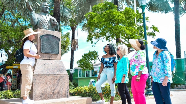 Guía hablando con un grupo de Visitantes junto a una estatua y un cartel Guía hablando con un grupo de Visitantes junto a una estatua y un cartel