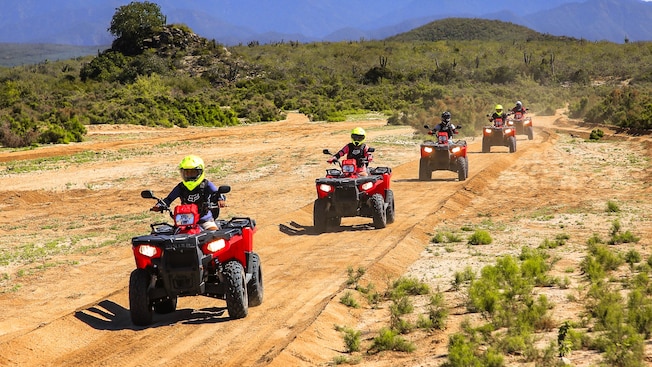 A group of riders on single seat all terrain vehicles driving single file in a desert setting A group of riders on single seat all terrain vehicles driving single file in a desert setting