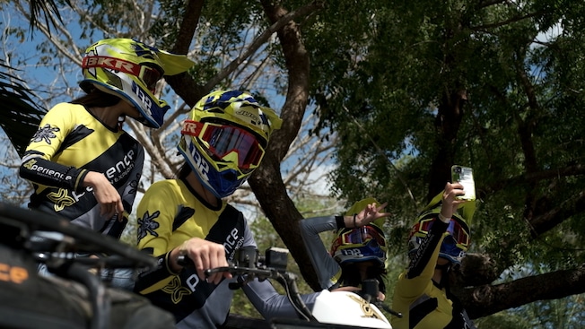 Duas pessoas usam capacete de segurança enquanto passeiam em quadriciclos ao lado de outras duas pessoas com capacete que posam para uma selfie Duas pessoas usam capacete de segurança enquanto passeiam em quadriciclos ao lado de outras duas pessoas com capacete que posam para uma selfie