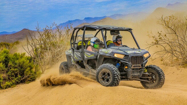 2 riders wearing helmets riding a 4 by 4 all terrain vehicle through the desert