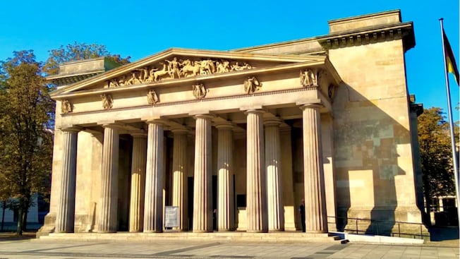 A neoclassical building with stone columns and engravings of a chariot battle scene A neoclassical building with stone columns and engravings of a chariot battle scene