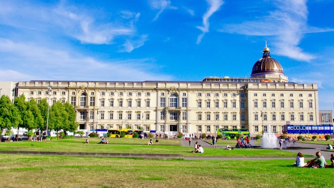 Um gramado do lado de fora do Humboldt Forum de Berlim, um enorme museu com muitas janelas e uma entrada abobadada Um gramado do lado de fora do Humboldt Forum de Berlim, um enorme museu com muitas janelas e uma entrada abobadada