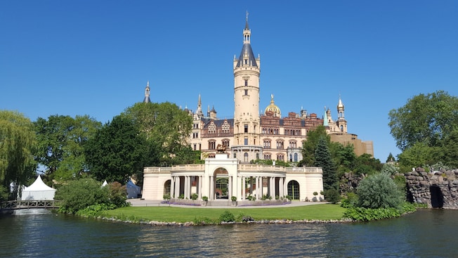 The entrance of Schwerin Castle overlooking a lake and surrounded by lush grounds The entrance of Schwerin Castle overlooking a lake and surrounded by lush grounds