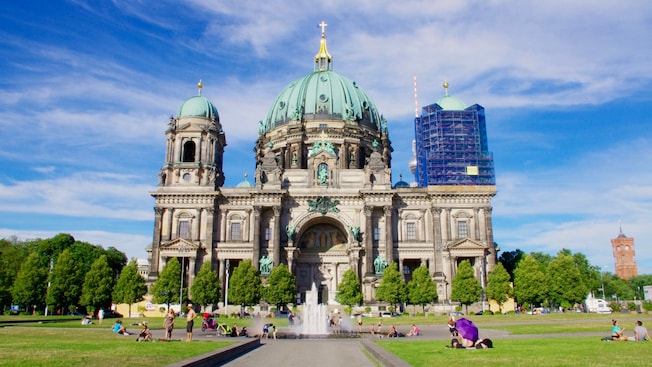 The entrance of the Berlin Cathedral with domed rooftops and ornately carved stone, overlooking a grassy lawn and fountain The entrance of the Berlin Cathedral with domed rooftops and ornately carved stone, overlooking a grassy lawn and fountain