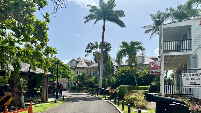 A road through Nelson's Dockyard, lined with buildings, posts, palm trees and cannons