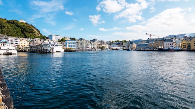 A body of water with buildings and a hill in the background in Alesund, Norway A body of water with buildings and a hill in the background in Alesund, Norway