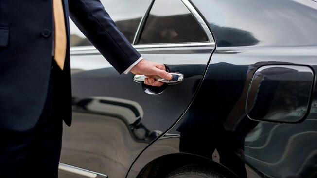 A private driver opening the door of a luxury sedan