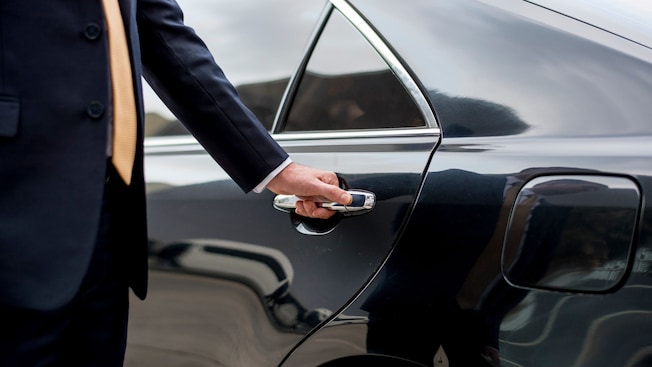 A private driver opening the door of a luxury sedan A private driver opening the door of a luxury sedan