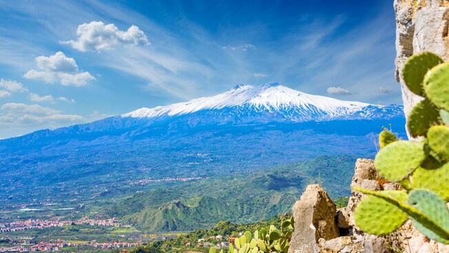 A snow capped volcano overlooks a city and farmland