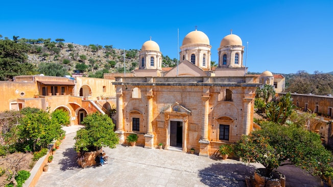 The stone façade of the Agia Triada Monastery reveals classic Greek architecture with columns, a pediment and 3 domes The stone façade of the Agia Triada Monastery reveals classic Greek architecture with columns, a pediment and 3 domes